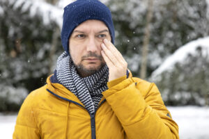 Young man having dry eyes health problem. Sick man in winter snow touching sensitive eye