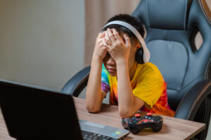 Asian boy sitting with his eyes closed while playing computer games online with game controller vision and vision problems in a child focusing on joystick controls.